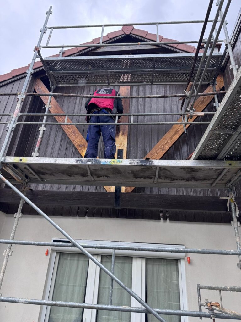 Artisan sur échafaudage devant une maison en rénovation extérieure