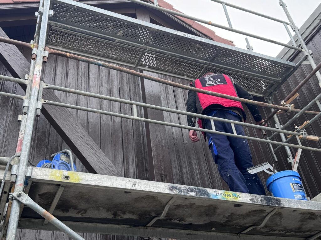 Artisan sur échafaudage devant un bardage bois en rénovation de façade