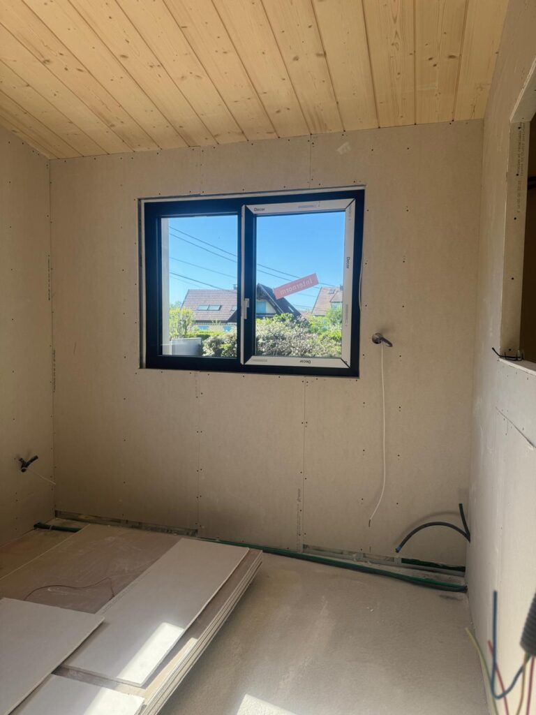 Pièce au plafond lambrissé avec fenêtre noire, chantier de rénovation